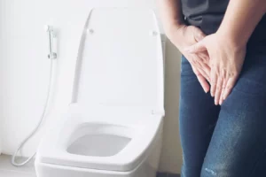 Imagem de uma pessoa com dor, representando sintomas comuns de infecção urinária, ao lado de um vaso sanitário.
