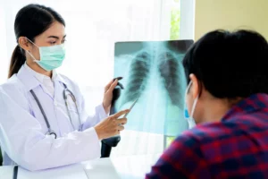 Médica analisa raio-x de pulmão com paciente, discutindo sintomas e diagnóstico de pneumonia.