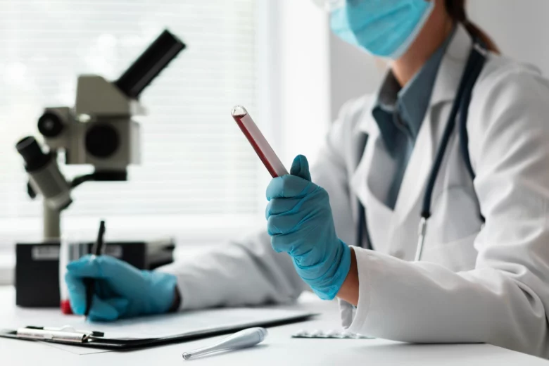 Profissional de saúde com jaleco, máscara, luvas e esteto realizando exame laboratorial com tubo de sangue em laboratório moderno.
