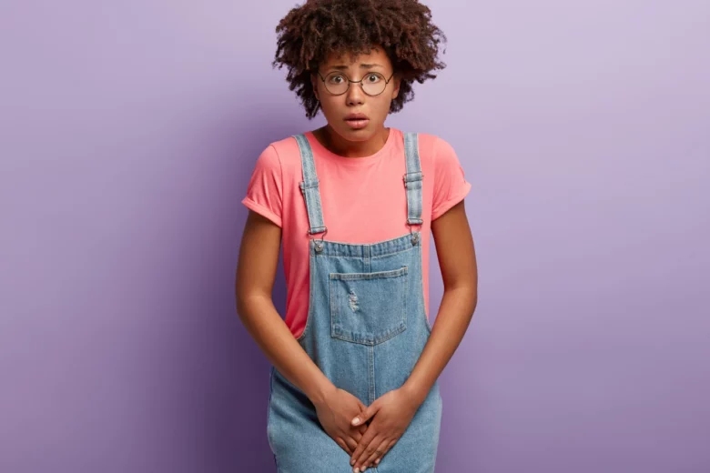 Mulher jovem com expressão de dor e desconforto, segurando a região genital, ilustrando sintomas de uma infecção urinária feminina.